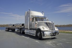 This is a photograph of a model semi type truck with flatbed trailer. It is hauling a load of steel pipe.